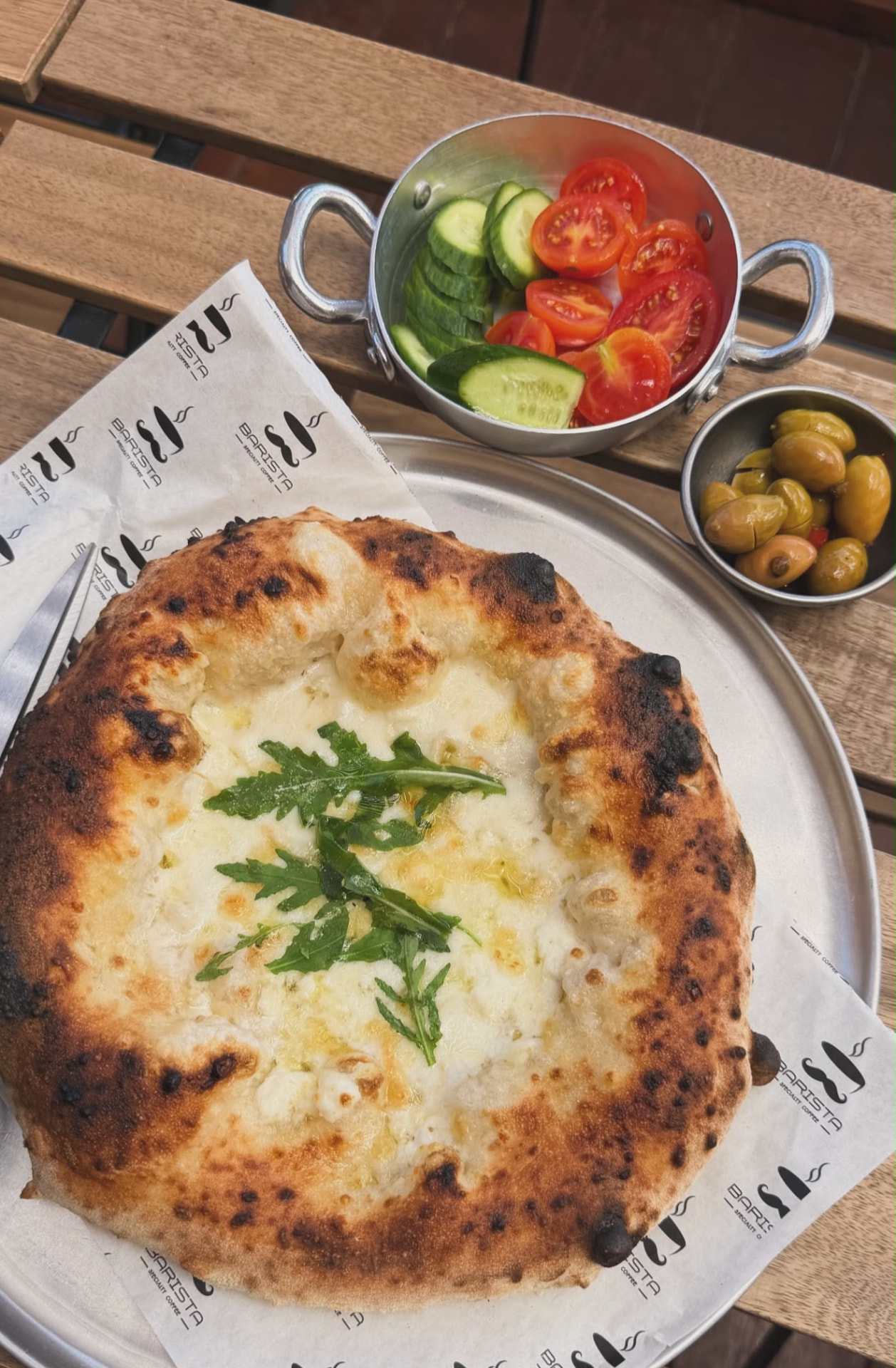 Wood-fired white pizza with rocket, served with olives and fresh salad